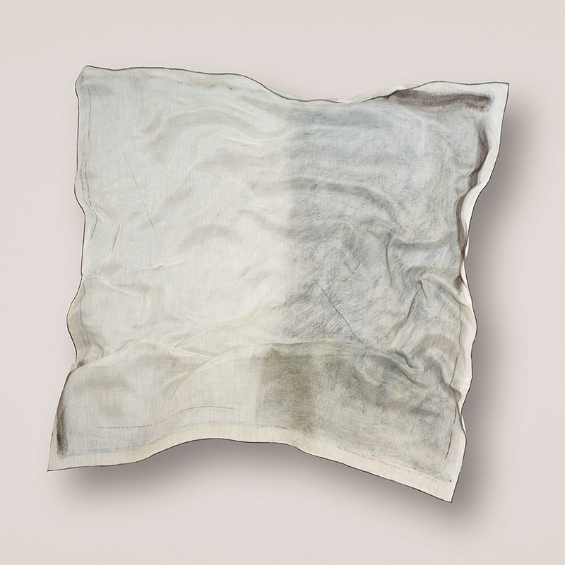 a large cashmere scarf seeming to float in front of a pale wall, the scarf has a subtle color and print from artist Dot Wade