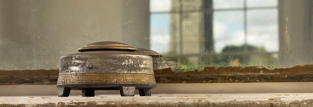 Jason Wason Textured Lidded vessel shown on a distressed fireplace mantle in front of a mirror reflecting the vessel and a castle outside