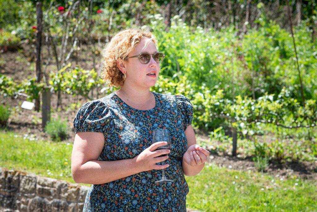 Sarah Marlowe Hall holding a glass of wine in a lush garden
