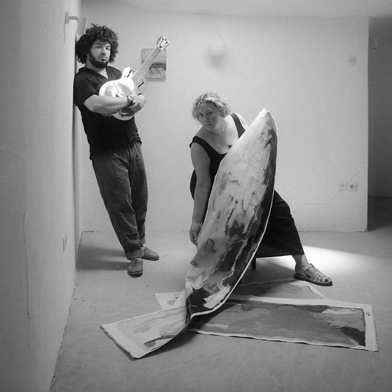 black and white photo of Zuk Zku and Sarah Marlowe Hall in as studio with guitar and painting